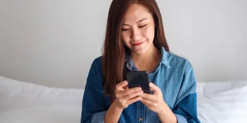 Seorang wanita sedang tersenyum melihat layar handphone