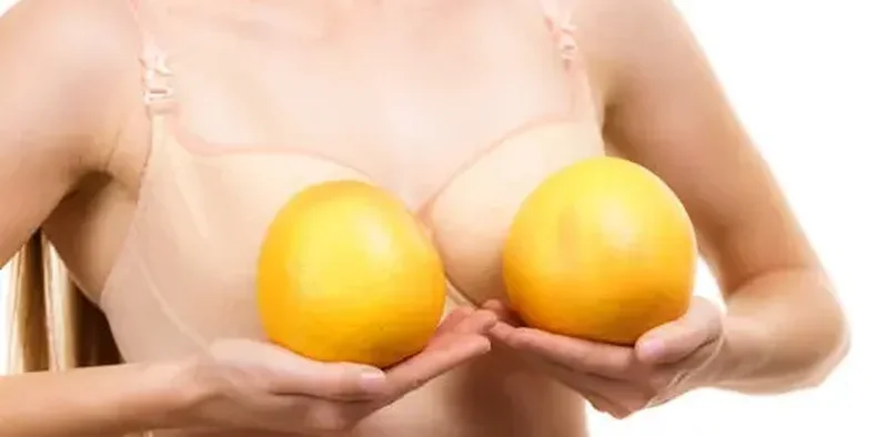 Wanita memegang dua jeruk di depan payudara