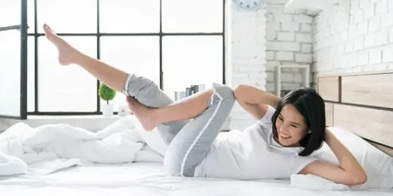 Seorang wanita sedang berolahraga di atas tempat tidur di pagi hari