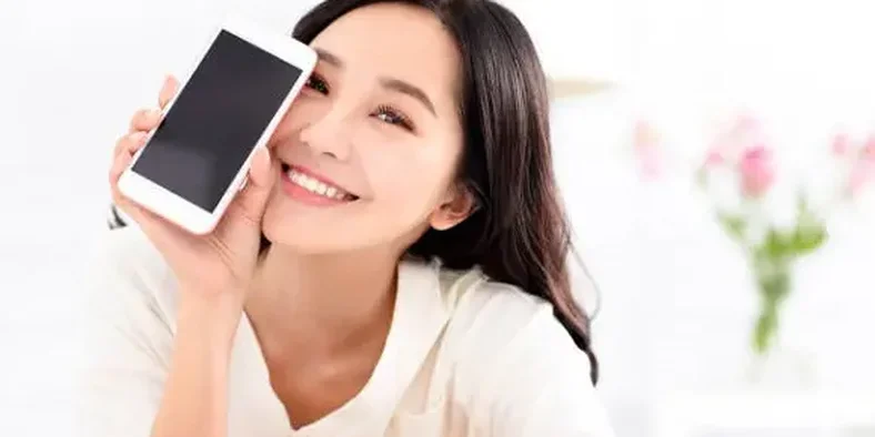 Wanita tersenyum memegang handphone
