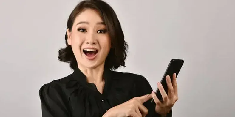 Wanita memegang handphone dengan wajah senang