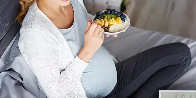 ibu hamil sedang memegang sendok dan piring berisi makanan
