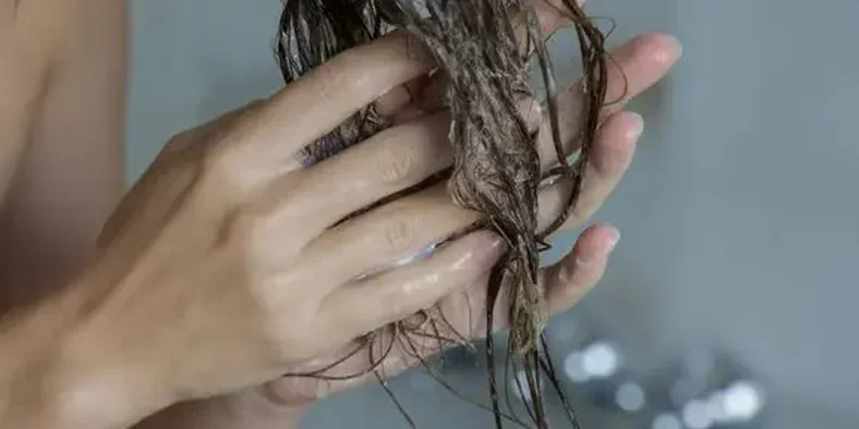 Perempuan sedang mencuci rambutnya menggunakan sampo