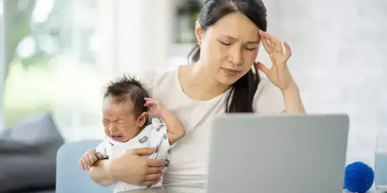 Ibu pusing di depan laptop sambil menggendong bayi