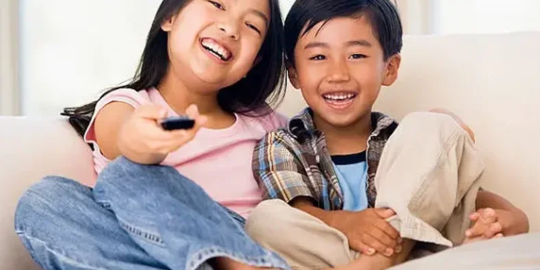 Dua anak sedang memegang remot TV sambil tersenyum