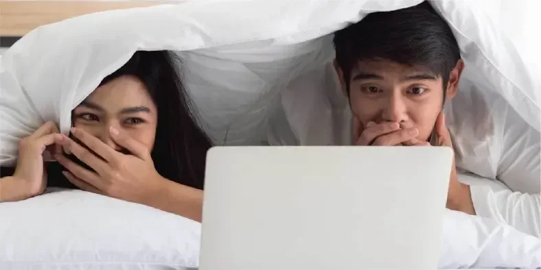 Wanita dan pria menonton film di ranjang