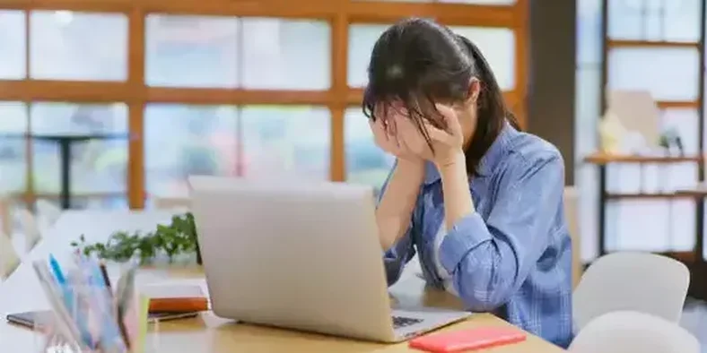perempuan sedih sambil menutup wajah di depan laptop
