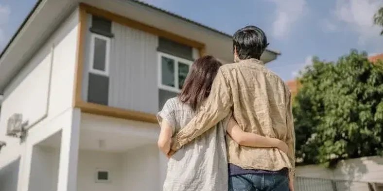sepasang suami istri menatap bangunan rumah