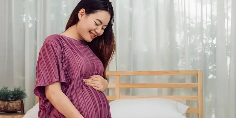 ibu hamil tersenyum ke arah perutnya