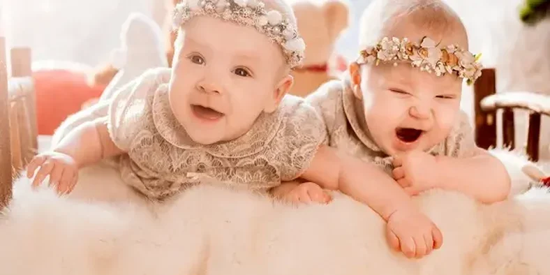 dua anak bayi sedang tertawa di atas tempat tidur