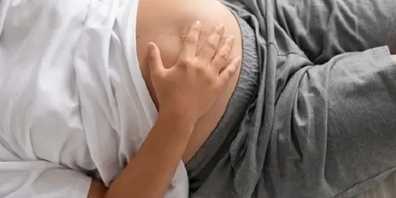 ibu hamil memegang perutnya sembari tidur di atas kasur