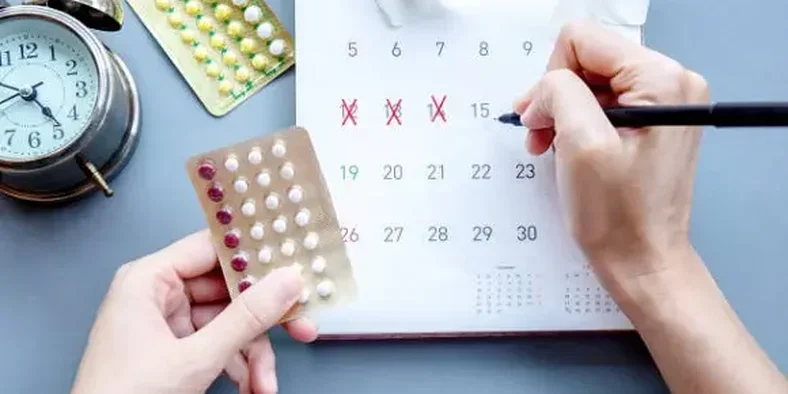Wanita menandai tanggal di kalender dan memegang pil KB