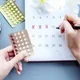 Wanita menandai tanggal di kalender dan memegang pil KB
