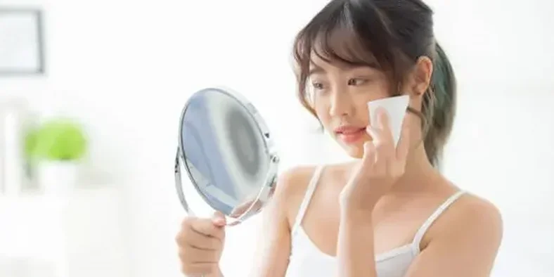 Wanita muda sedang membersihkan wajah dengan kapas