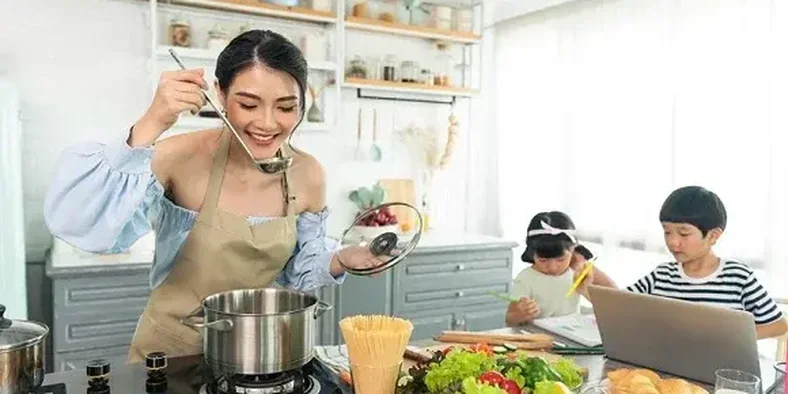 Ibu muda sedang memasak sambil menemani anaknya